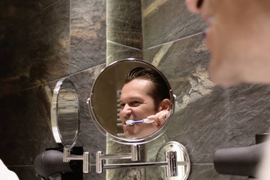 Banyoda diş fırçalayan bir adamın aynadaki yansıması..