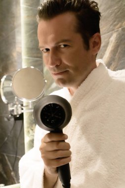 Adam banyoda saç kurutma makinesi kullanıyor ve kameraya bakıyor.. 