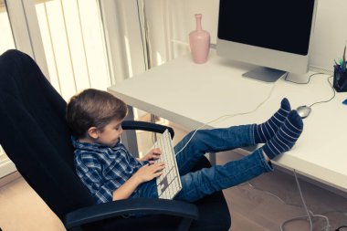 Masaüstü bilgisayarında internette sörf yaparken bilgisayar klavyesinde yazan küçük çocuk..