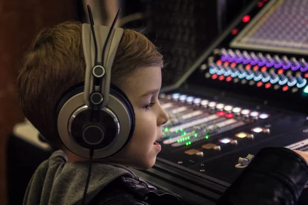 Small boy with headphones editing music on sound mixing desk in a studio.