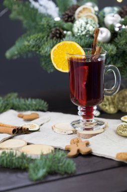 Kışlık ikramlar, portakallı bir kupa sıcak şarap, ve kurabiyeler, ahşap kahverengi bir masanın üzerindeki malzemeler. Noel için geleneksel sıcak içecek, arka planda Noel kompozisyonu.