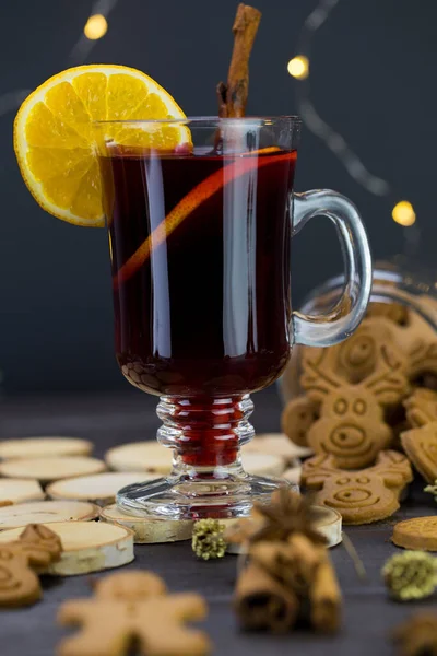 Mug of warm wine with orange, cookies and cinnamon, hot drink for Christmas, on a wooden stand.