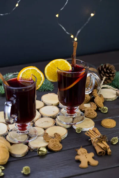 Mugs of warm wine with orange, cookies and cinnamon, hot drink for Christmas, on a wooden stand.