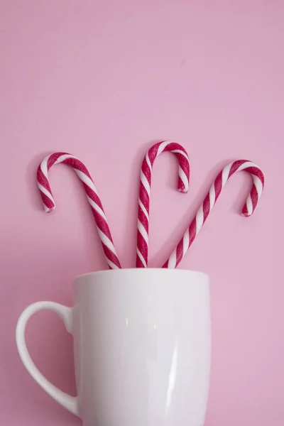 in a mug of Christmas candy cane, on a pink background.