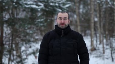 Dış giysili yakışıklı bir adamın portresi. Arka planda karla kaplı bir ormanda durup kameraya bakıp gülümsüyor..