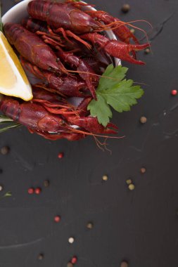 Lezzetli haşlanmış kerevit, biber, limon ve maydanozlu taş tabakta yakın plan. Metnin için boş yer. Siyah arkaplan.