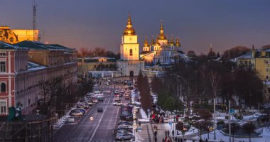 Ukrayna 'nın başkenti Kyiv' deki Sofya Meydanı 'nın kış akşamı manzarasında, gün batımında koyu mavi gökyüzü ve tarihi kent mimarisine karşı sıcak ışık altında parlayan Aziz Michaels Altın Kubbe Manastırı yer alıyor..
