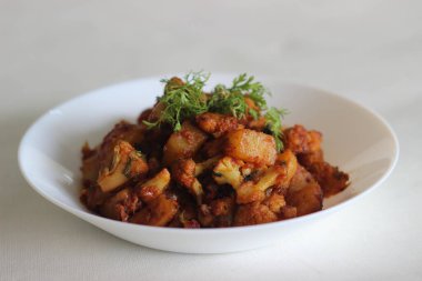 Karnabahar patatesi soğan, domates ve baharatla sotelenmiş Hint ekmeği ile servis edilir.