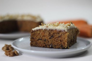 İnce bir kat tereyağı, şeker ve ezilmiş cevizle kaplı havuçlu cevizli kek dilimi. Beyaz arkaplanda havuçla fotoğraflanmış.