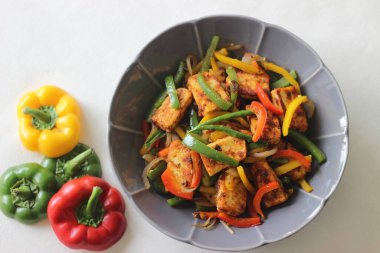 Tawa kızarmış paneer ve sotelenmiş dolma biber. Başlangıç yemeği olarak lezzetli bir karışım. Beyaz arka planda çiçek şeklinde bir kasede fotoğraflanmış.