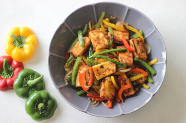 Tawa kızarmış paneer ve sotelenmiş dolma biber. Başlangıç yemeği olarak lezzetli bir karışım. Beyaz arka planda çiçek şeklinde bir kasede fotoğraflanmış.