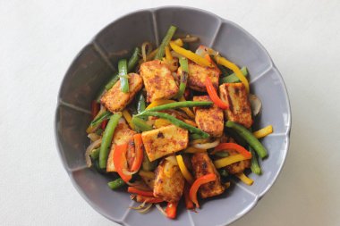 Tawa kızarmış paneer ve sotelenmiş dolma biber. Başlangıç yemeği olarak lezzetli bir karışım. Beyaz arka planda çiçek şeklinde bir kasede fotoğraflanmış.