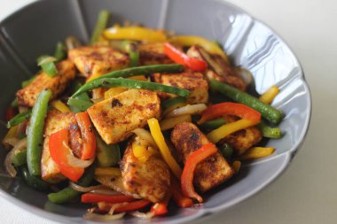 Tawa kızarmış paneer ve sotelenmiş dolma biber. Başlangıç yemeği olarak lezzetli bir karışım. Beyaz arka planda çiçek şeklinde bir kasede fotoğraflanmış.