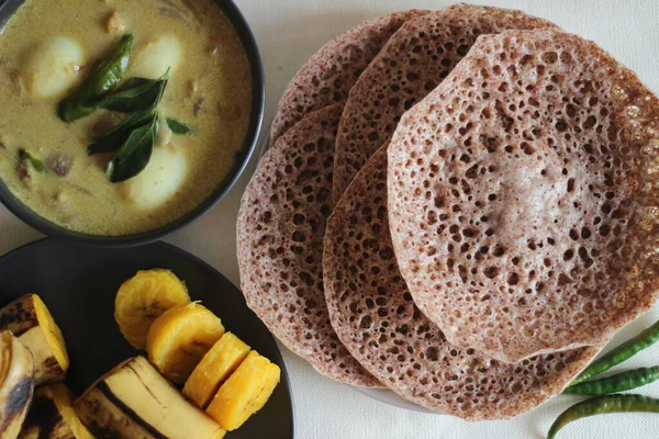 Hoppers made of finger millet served with egg stew prepared in Kerala style and steamed plantain. Shot on white back ground