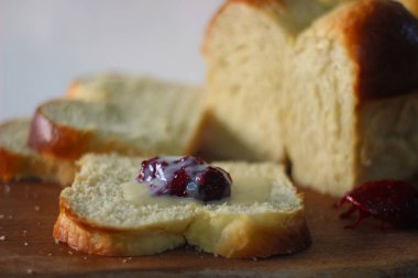 Taze pişmiş Brioche ekmeği dilimlenmiş ve ahşap bir tahtanın üzerinde duruyor. Reçelle servis edilmiş. Beyaz arkaplanda çekilen.