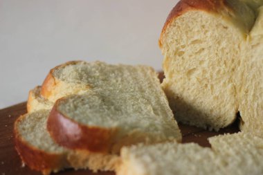 Taze pişmiş Brioche ekmeği dilimlenmiş ve ahşap bir tahtanın üzerinde duruyor. Beyaz arkaplanda çekilen.