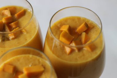 Mango smoothie, olgun ve tatlı mango parçaları, soğuk süt, yoğurt ve şekerin karışımı ile hazırlanmış soğuk ve cezbedici bir mango meyve suyu. Şarap bardağında servis edilmiş. Beyaz arkaplanda çekilen