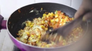 Yumurtayla mısırı karıştırmak, pişen kişinin arkasından sapsız tavaya havuç atmak. Tipik bir Hint mutfağının içinde.