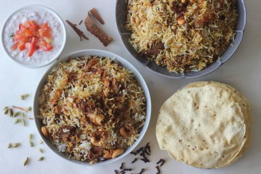 Koyun Biryani. Baharatlarla pişirilmiş hafif baharatlı ghee pilavı ile bol karamelli soğan ve yoğurt içinde marine edilmiş koyun eti karışımı bir yemek. Papad ve curd ile servis edilir..