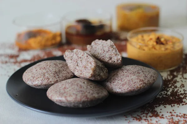 Steamed cakes made with finger millets and skinned black gram. Locally known as Ragi idli. Served along with coconut chutney, sambar and red fish curry. Shot on white background.