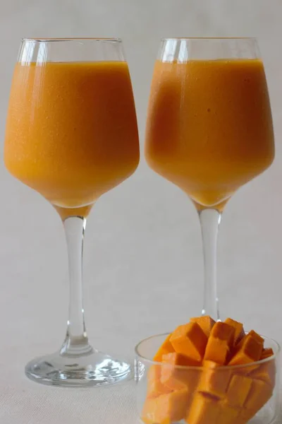 Two glasses of mango juice with nicely sliced mango kept beside. Shot on white background.
