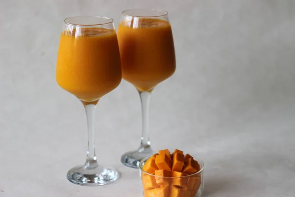 Two glasses of mango juice with nicely sliced mango kept beside. Shot on white background.