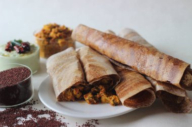 Mayalanmış tahıllı parmak darı hamurundan yapılmış çıtır krep. Krep ve hindistan cevizi sosunun ortasında süzme peynir sosuyla servis ediliyor. Beyaz arkaplanda çekilen.