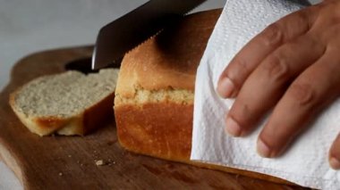 Kahvaltıda odun kesme tahtasıyla ev ekmeğini dikkatlice dilimliyorum. Beyaz arkaplanda çekilen.