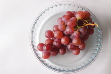 Kırmızı masa üzümleri cam bir kasede, içinde Red Globe, Crimson Seedless veya Flame Seedless var. Dolgun, parlak meyve temaları beslenme, tazelik ve minimalist natüralizm için idealdir.