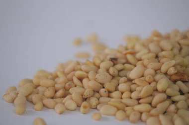 Çam fıstığı, aynı zamanda çam çekirdekleri olarak da bilinir, temiz bir yüzey üzerinde kabuklu tohumlar içeren gevşek bir yığın halinde sunulur. Pesto ve pişirme için Akdeniz mutfağında sıkça kullanılan pürüzsüz dokuyu vurgulayan yakın çekim yiyecek görüntüsü