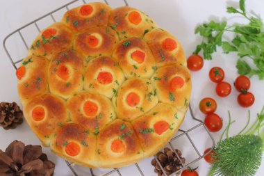 Çeri domates ve şifalı otlarla kaplı taze pişmiş ekmekler soğutma rafına dizilmiş. İnce bir bayram dekoruyla süslenmiş, sıcak bir Noel ve kış yemeği ortamı yaratıyor.