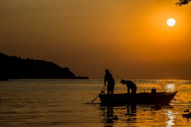 Gün batımının muhteşem renklerinin denize yansıdığı harika bir fotoğraf. Teknedeki balıkçıların siluetleri doğanın ve insanın büyük uyumunu sembolize ediyor..