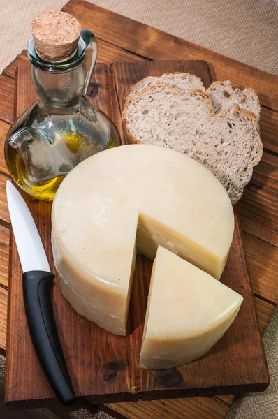 Queso, aceite, pan y un cuchillo en una tabla de madera — Foto de Stock