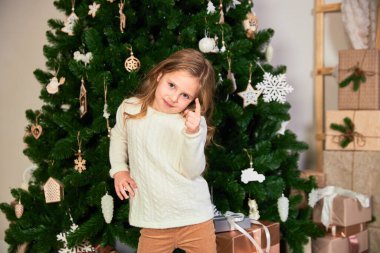 Beyaz eko elbiseli bir kız Noel kızı gibi giyinmiş. Arkada yeşil bir Noel ağacı ve hediyeler var. Kameradaki kız noktaları.