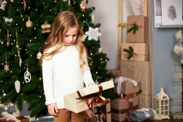 Dziewczyna stoi w pokoju z zielonym świerkiem, dziewczyna otrzymała prezent na Boże Narodzenie, dziewczyna zdenerwowany i patrzy na prezent — Zdjęcie stockowe