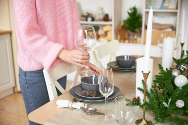 Kadın, aile tatili için beyaz mutfakta sadece elleri ve yüzü olmayan bir Noel masası servis ediyor.