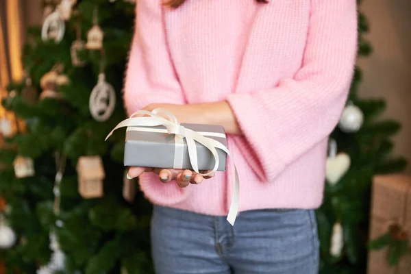Mujer sostiene gris regalo de Navidad en medio del árbol de Navidad decorado para las vacaciones —  Fotos de Stock