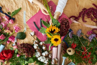 Düz kompozisyon çiçekçisi el işi kağıt ve pembe arka plan kağıdı üzerinde bir buket oluşturur.