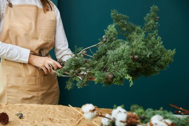 Dişi bir çiçekçi çelenk ya da ladin, koni ve çiçekten bir buket yapar.