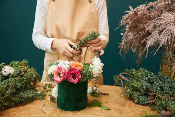 A female florist creates a bouquet for Christmas from flowers and branches of spruce. The work of a florist.