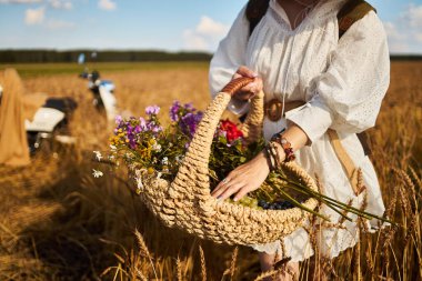 Bir kadın elinde yaz çiçekleri olan bir sepet tutuyor.