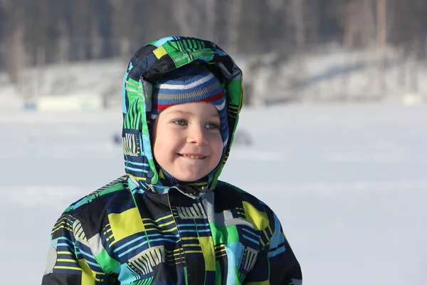 Das lächelnde Kind in einer farbigen Jacke mit Kapuze gegen Schnee — Stockfoto