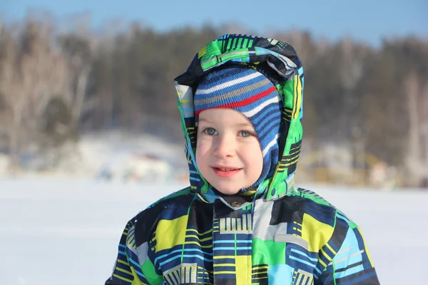 Das überraschte Kind in einer farbigen Jacke mit Kapuze gegen den Schnee — Stockfoto