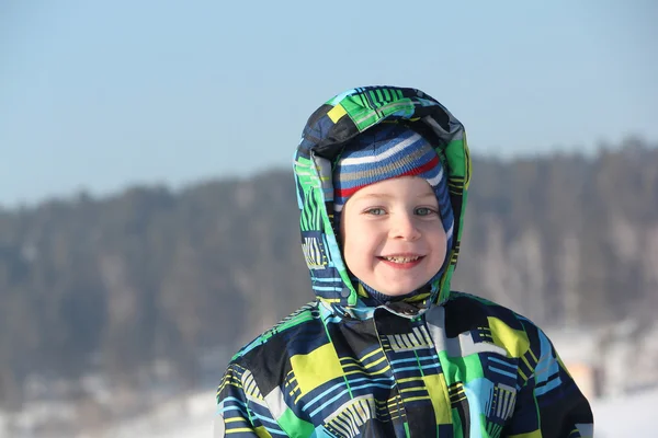 Das glückliche Kind in einer farbigen Jacke gegen Himmel und Schnee — Stockfoto