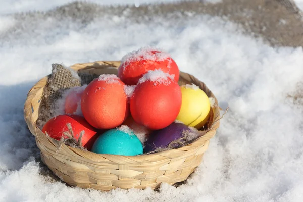 Color Easter eggs in a wooden basket on a napkin in snow — Stock Photo, Image