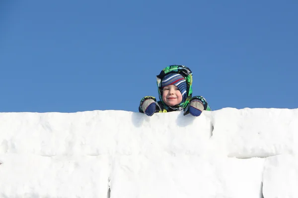 Šťastné dítě v barevné sako na vrcholu zdi od sněhové bloky — Stock fotografie