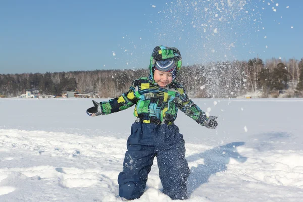 De kleine jongen in een kleur jas met een capuchon gooit sneeuw — Stockfoto