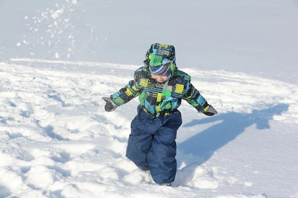 Der kleine Junge in der farbigen Jacke mit Kapuze wirft Schnee — Stockfoto