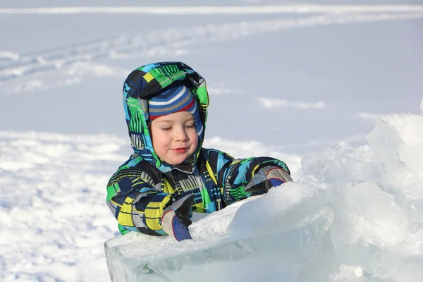 De kleine jongen in een kleur jas het stuk ijs in de hand te houden — Stockfoto