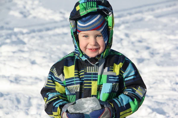De kleine jongen in een kleur jas het stuk ijs in de hand te houden — Stockfoto